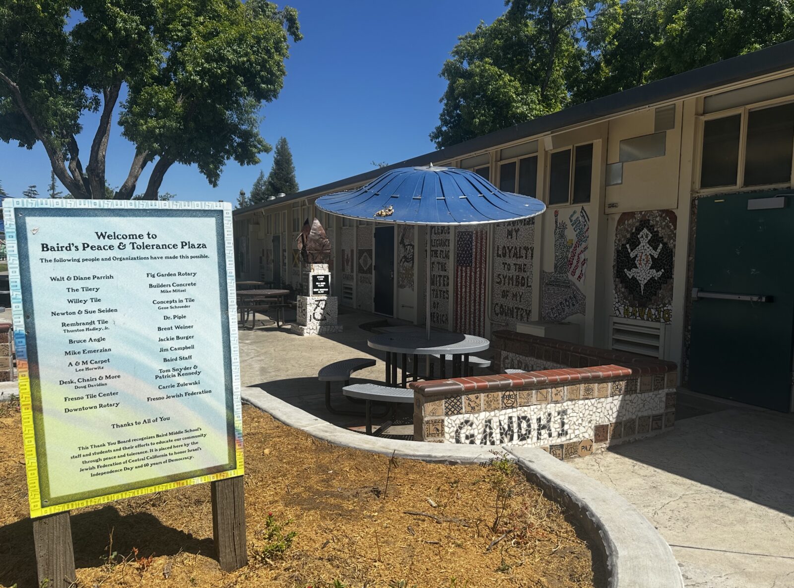 Entrance sign for Baird's Peace and Tolerance Plaza, with the Gandhi tribute wall behind it